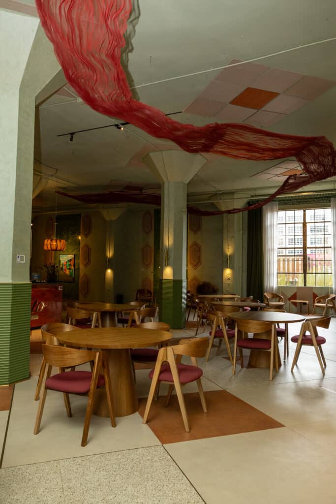 Comedor con mesas redondas de madera, sillas y una instalación roja suspendida